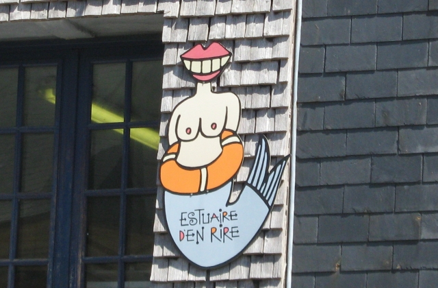 a sign outside a fish cafe in honfleur showing half naked woman half fish and no head just a smile